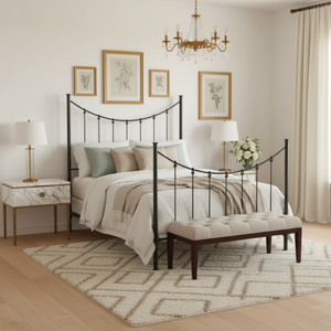 A black metal bed frame with a curved headboard and footboard stands in a bright, neutral-toned bedroom with light wood floors, a round woven rug, bedside tables with lamps, and a small plant.