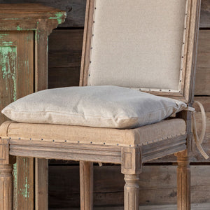 A rustic wooden dining chair with a beige linen seat cushion and a matching back cushion, styled next to a distressed green wooden cabinet.