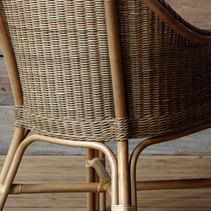 Close-up of a woven rattan chair showing the backrest, armrest, and natural wood frame on a wooden floor.