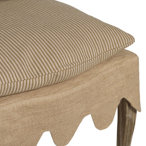 Close-up of a beige upholstered stool or ottoman with a striped cushion, a burlap-style skirt, and a visible wooden leg on a white background.
