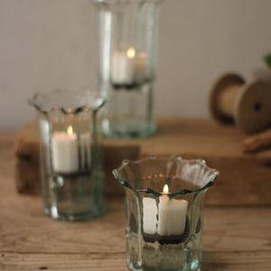Three glass candle holders with candles on a wooden surface.
