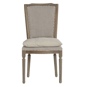 A classic high-back dining chair with a distressed gray-brown wood frame, featuring light beige fabric upholstery on the backrest and seat cushion, accented with silver nailhead trim.