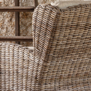 Close-up of a woven rattan armchair or outdoor chair showing the detailed texture of the natural wicker and a light beige cushion.