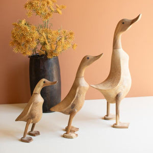 Three hand-carved wooden ducks styled with a vase of flowers