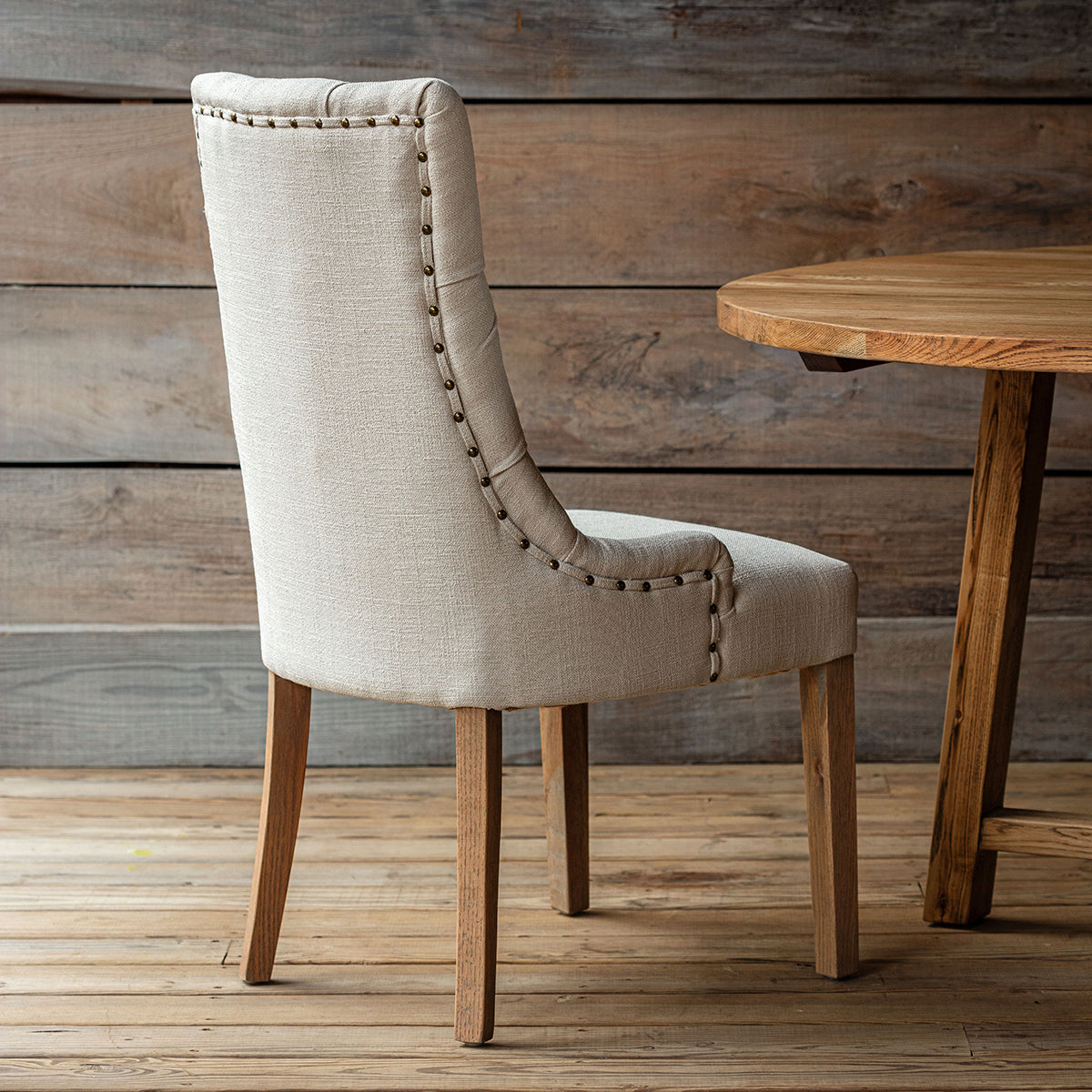 Beige upholstered chair with wooden legs in front of a wooden table against a wooden wall.