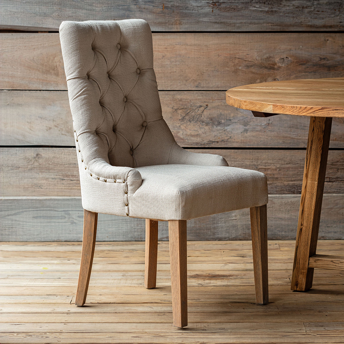 Beige upholstered chair with wooden legs in front of a wooden table against a wooden wall.