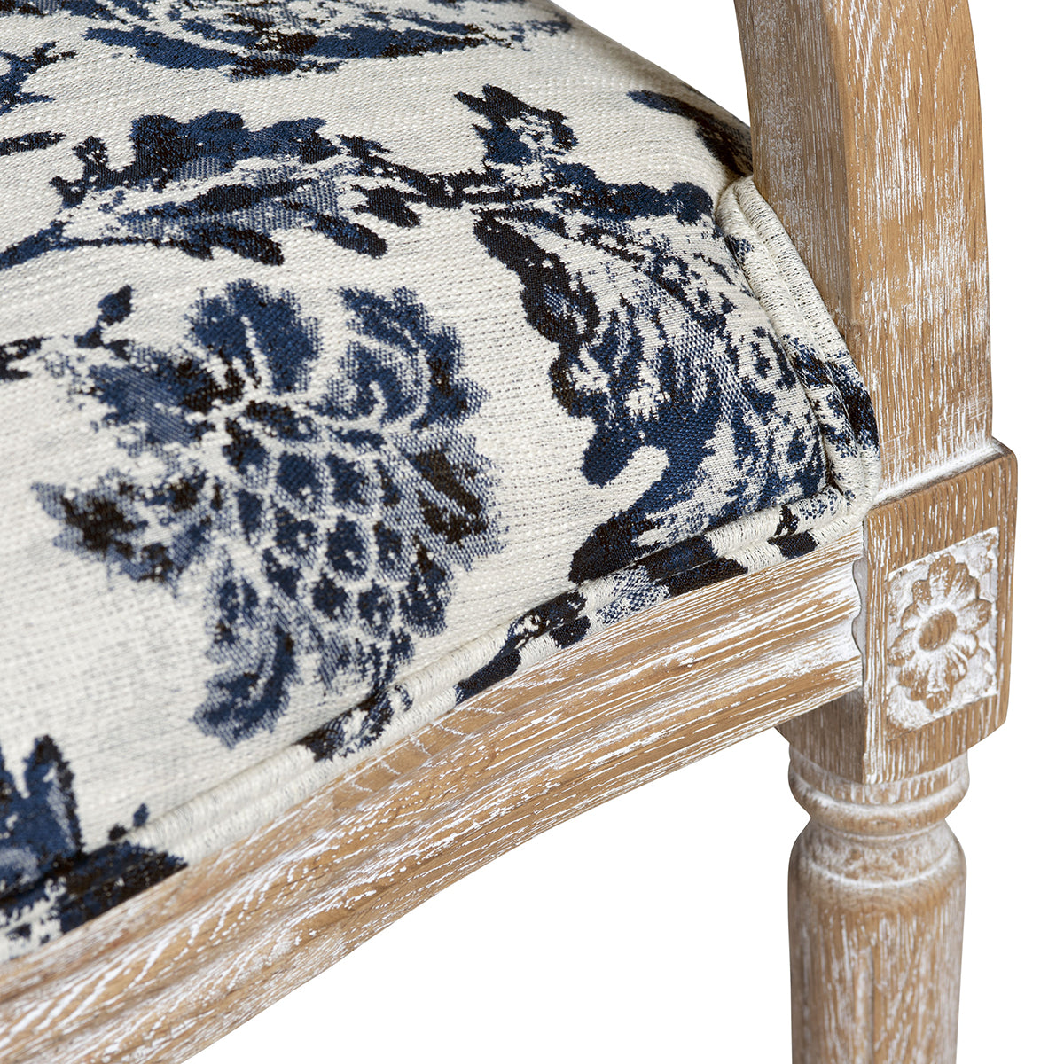 Close-up of a chair corner showing a distressed light wood frame and upholstered seat with a blue and cream floral pattern.
