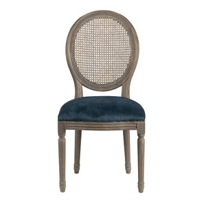 An oval-back dining chair with a distressed gray-brown wood frame, a woven cane backrest, and a deep navy blue velvet upholstered seat, shown against a plain white background.