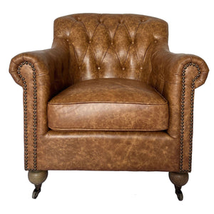 A classic Chesterfield armchair upholstered in distressed brown leather, featuring tufted button detailing on the backrest, rolled arms with nailhead trim, and dark wooden legs with casters. The chair is shown against a plain white background with a model number and dimensions printed below.