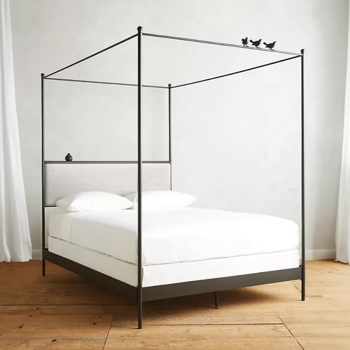 Black metal canopy bed with white bedding on a wooden floor.