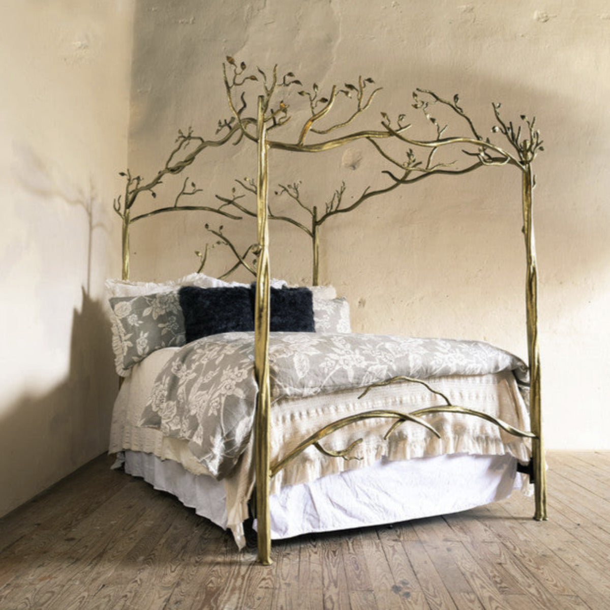 A canopy bed with a hand-forged iron frame featuring a leafy branch design and a white mattress.
