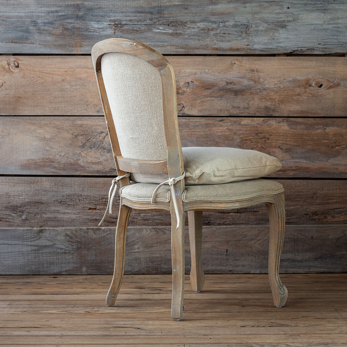 Vintage-style chair with beige cushion against a wooden wall.