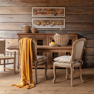 Wooden dining table with chairs and a yellow cloth in a rustic setting.