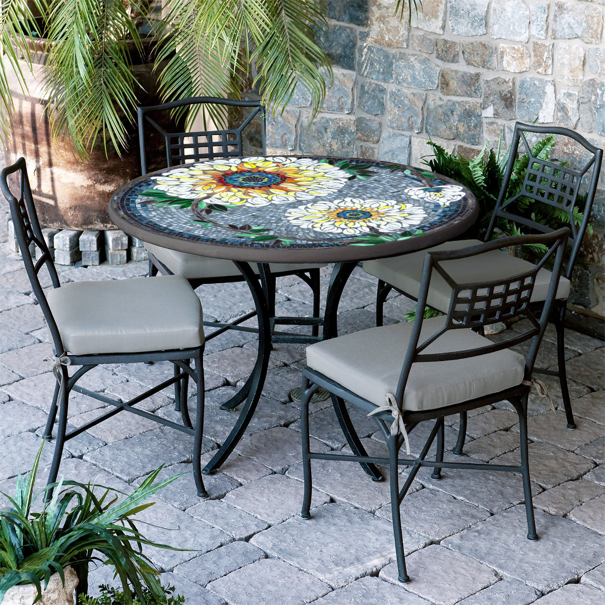 A round Florasol mosaic patio table with a colorful floral pattern on the tabletop, surrounded by four chairs with cushions.