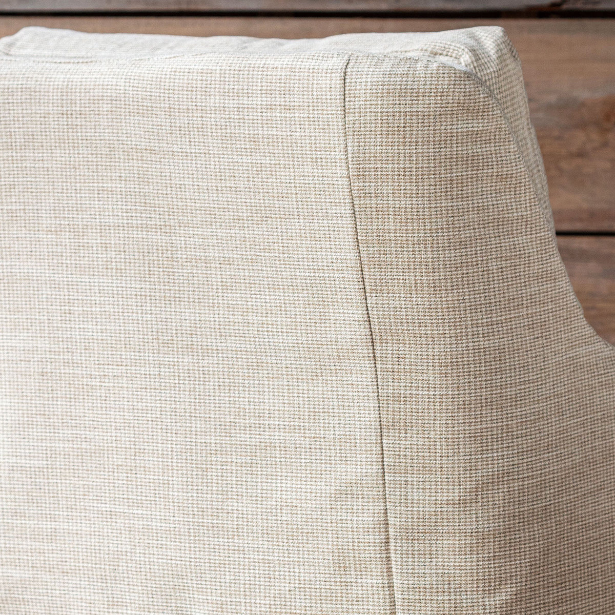 Close-up of a textured beige fabric cushion with a visible seam, resting on a rustic wooden surface.