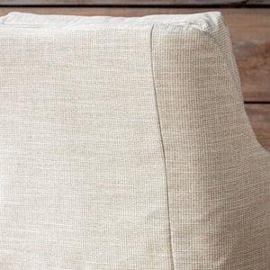 Close-up of a textured beige fabric cushion with a visible seam, resting on a rustic wooden surface.