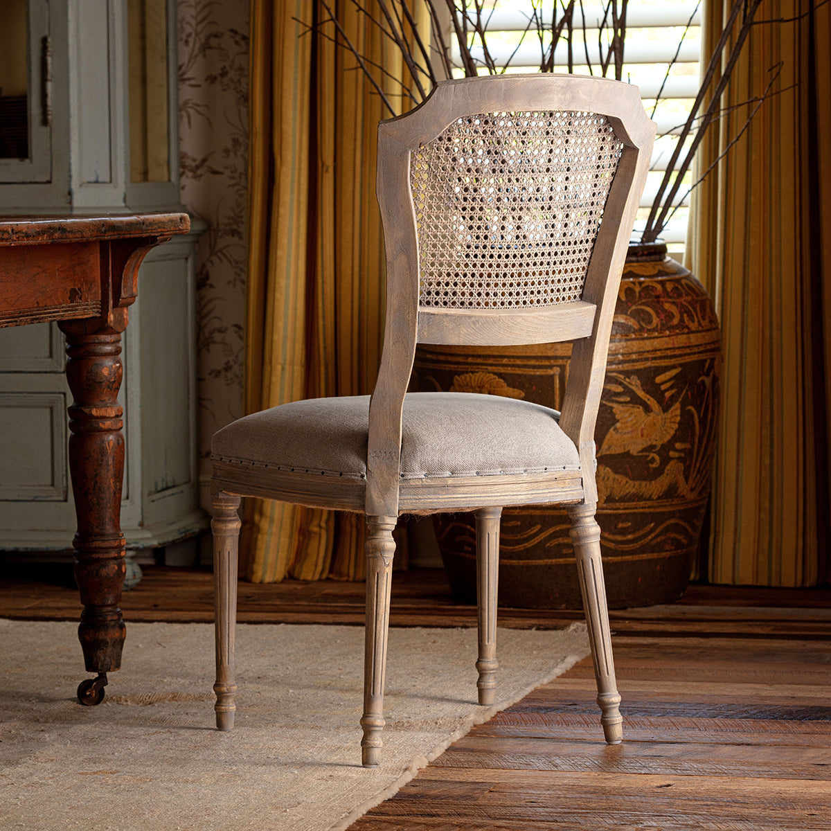 Chair with a woven backrest in a room with wooden furniture and yellow curtains.