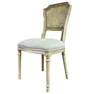 A distressed vintage-style side chair with a light beige upholstered seat, a woven cane backrest, and a weathered gold/cream painted frame, shown on a white background with a model number in the bottom left corner.