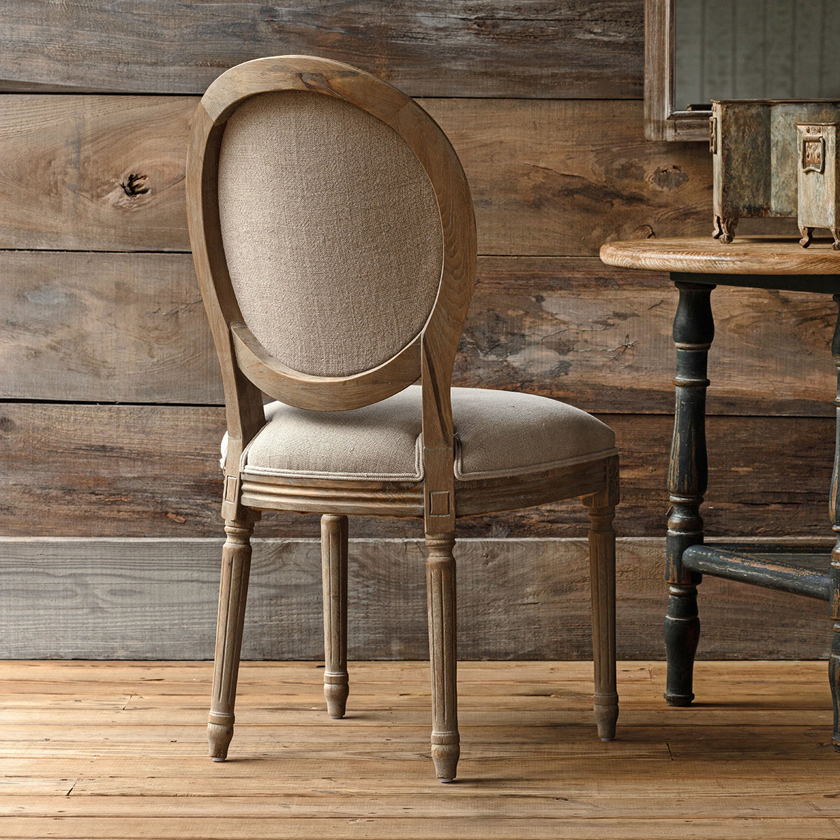 Wooden chair with beige cushion against a rustic wooden wall.