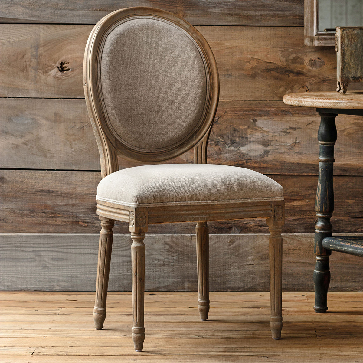 Wooden chair with beige cushion against a rustic wooden wall.