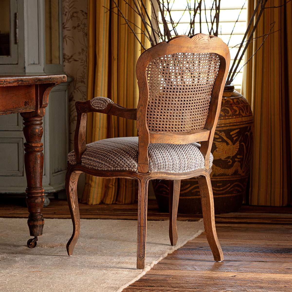 Wooden chair with wicker backrest and patterned cushion in a room with a table and decorative items.