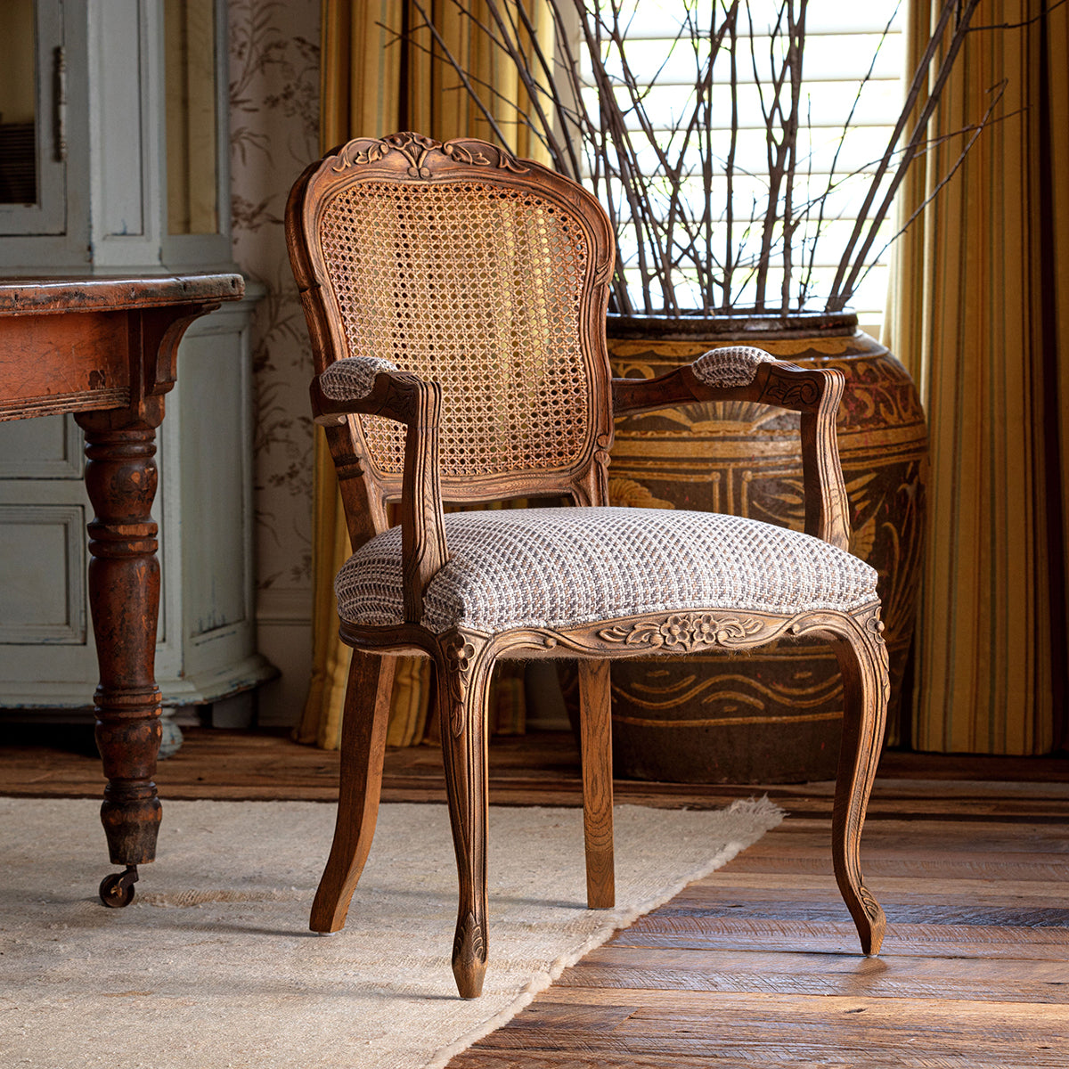 Wooden chair with wicker backrest and patterned cushion in a room with a table and decorative items.