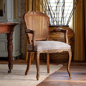 Wooden chair with wicker backrest and patterned cushion in a room with a table and decorative items.