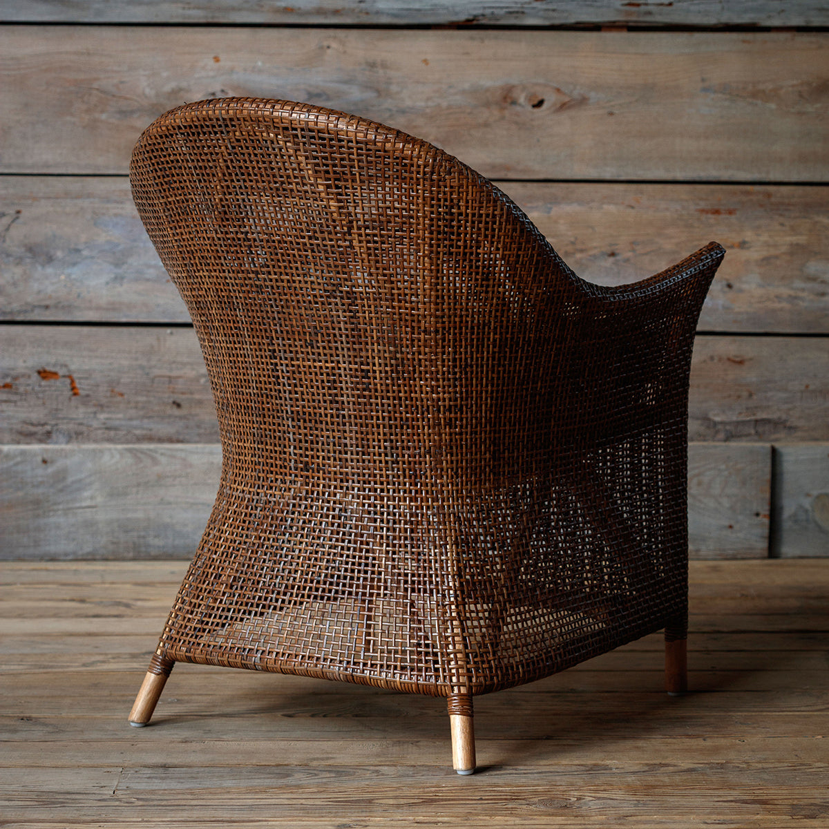 Wicker armchair with a cushion against a wooden wall.