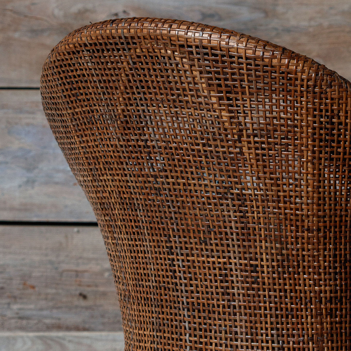 Close-up of a brown woven rattan chair back, showing the detailed texture of the hand-woven material against a rustic wooden plank background.