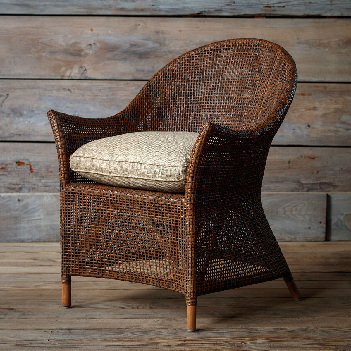 Wicker armchair with a cushion against a wooden wall.