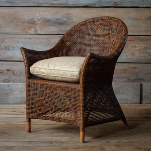 Wicker armchair with a cushion against a wooden wall.