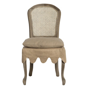 A classic French chaise dining chair with a distressed gray-brown wood frame, a woven cane backrest, a striped beige cushion, and a matching fabric skirt with a scalloped edge.