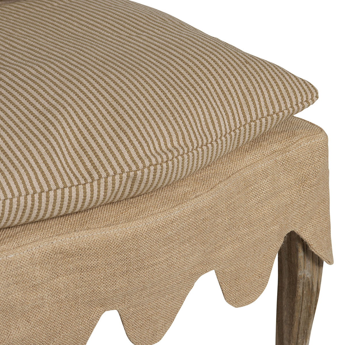 Close-up of a beige upholstered stool or ottoman with a striped cushion, a burlap-style skirt, and a visible wooden leg on a white background.