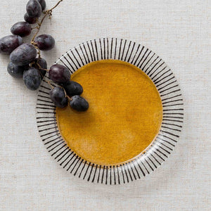A round ceramic plate with a black radial stripe border, surrounding a golden yellow center.