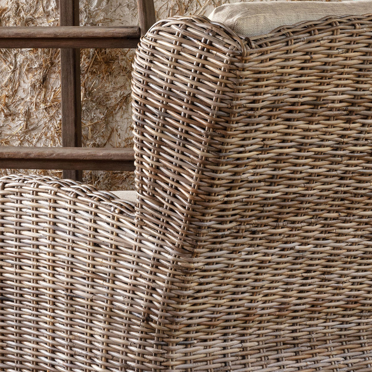 Close-up of a woven rattan armchair or outdoor chair showing the detailed texture of the natural wicker and a light beige cushion.