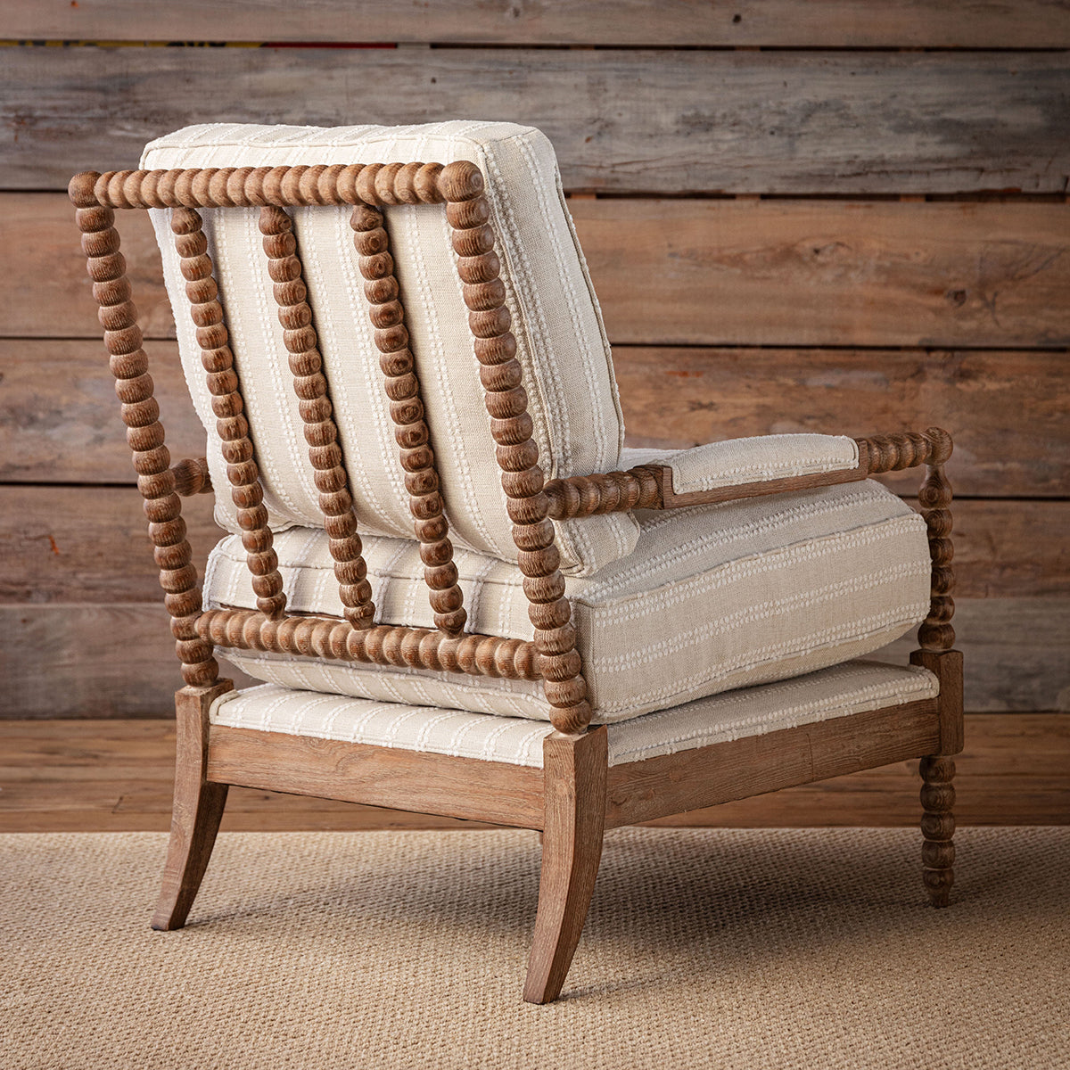A rustic spindle-back accent chair with cream and beige striped upholstery, set against a weathered wood plank wall on a jute rug.