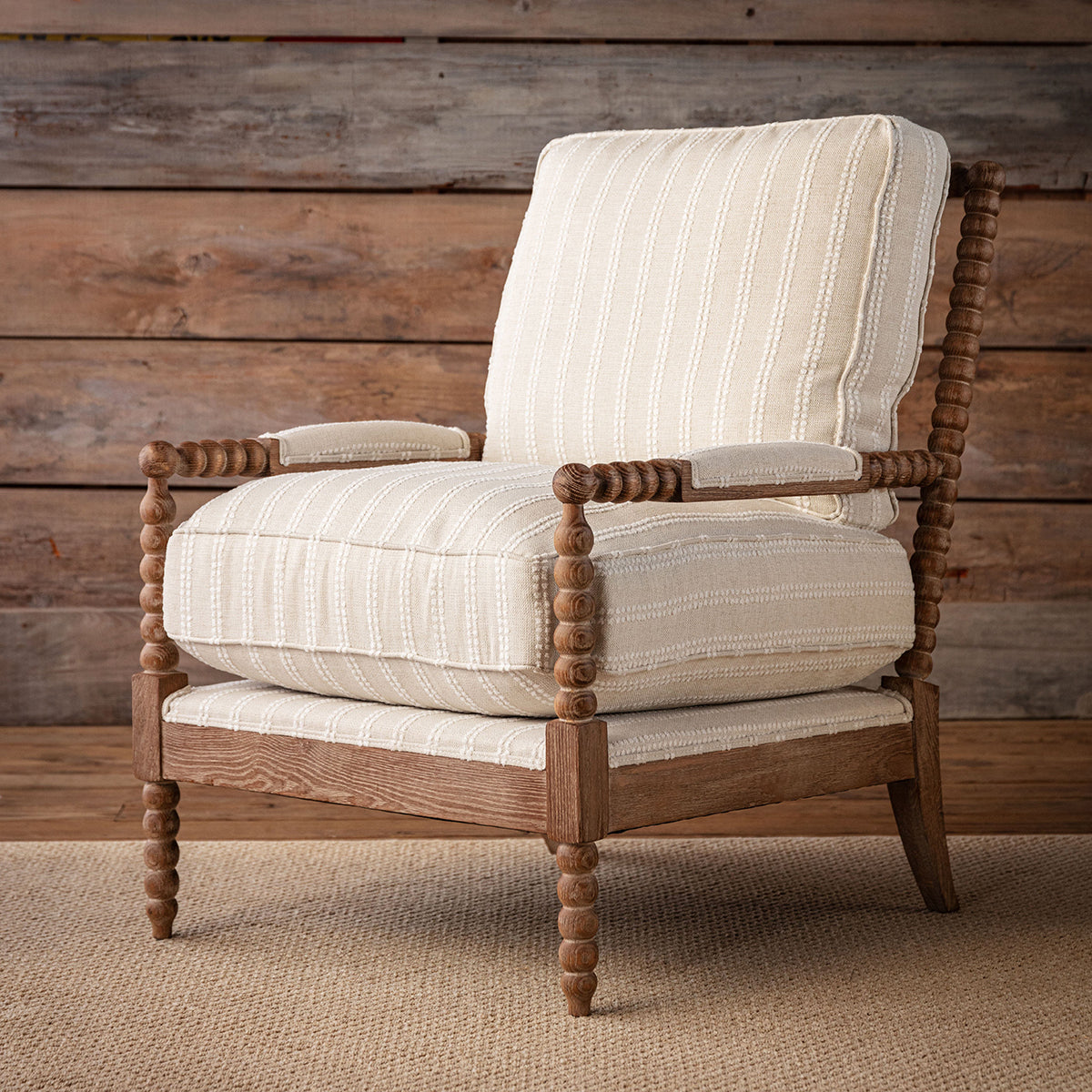 A rustic spindle-back accent chair with cream and beige striped upholstery, set against a weathered wood plank wall on a jute rug.