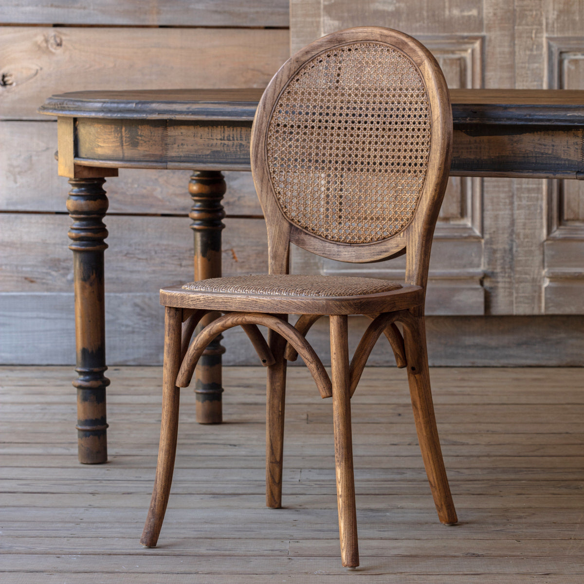 Bellhaven Cane Back Dining Chair beside a rustic wood desk, showing its oval cane back and bentwood frame