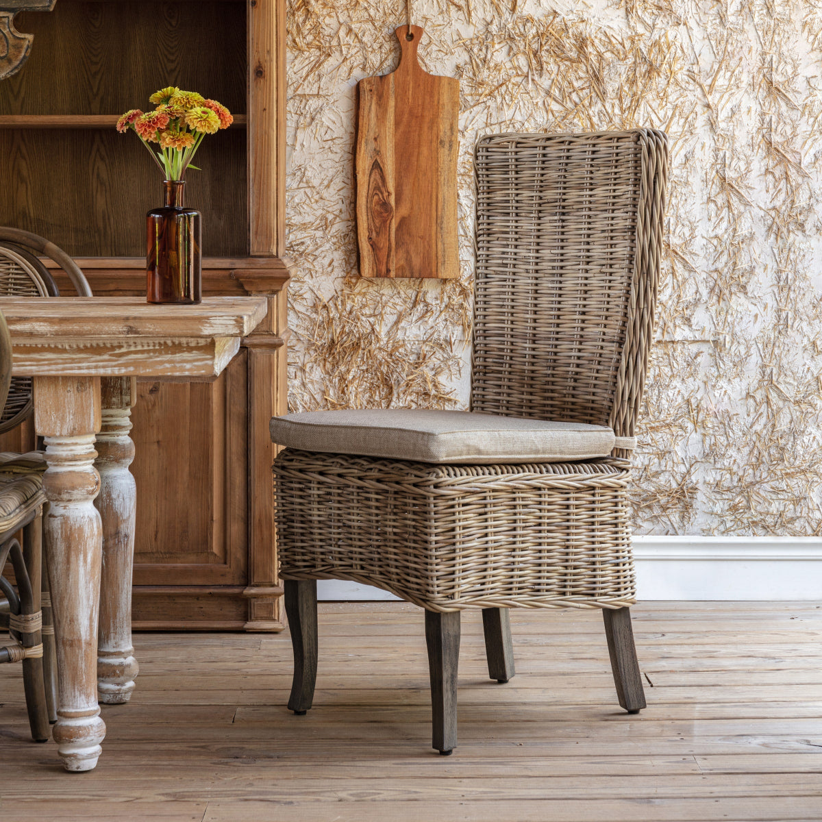 Copperfield Rattan Dining Chair with a tall woven back and linen cushion beside a rustic dining table