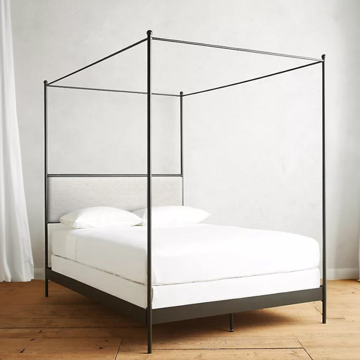 Elowen hand-forged iron canopy bed with a slender black frame, upholstered headboard and white bedding