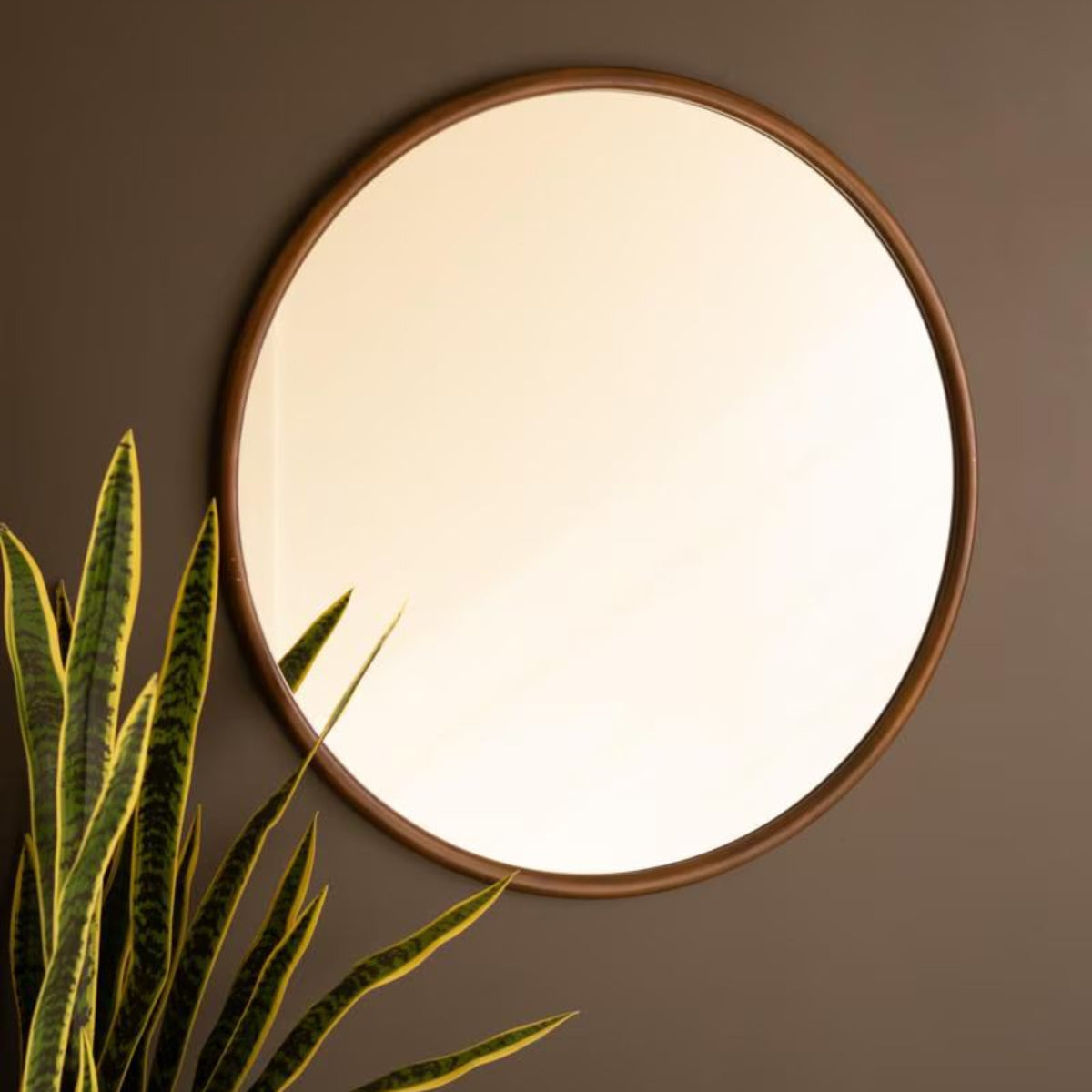 Round wood framed mirror on a dark wall with ornamental grass