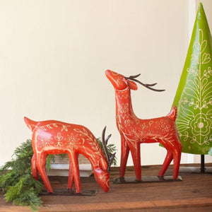 Red folk art reindeer pair displayed on a wood shelf with greenery