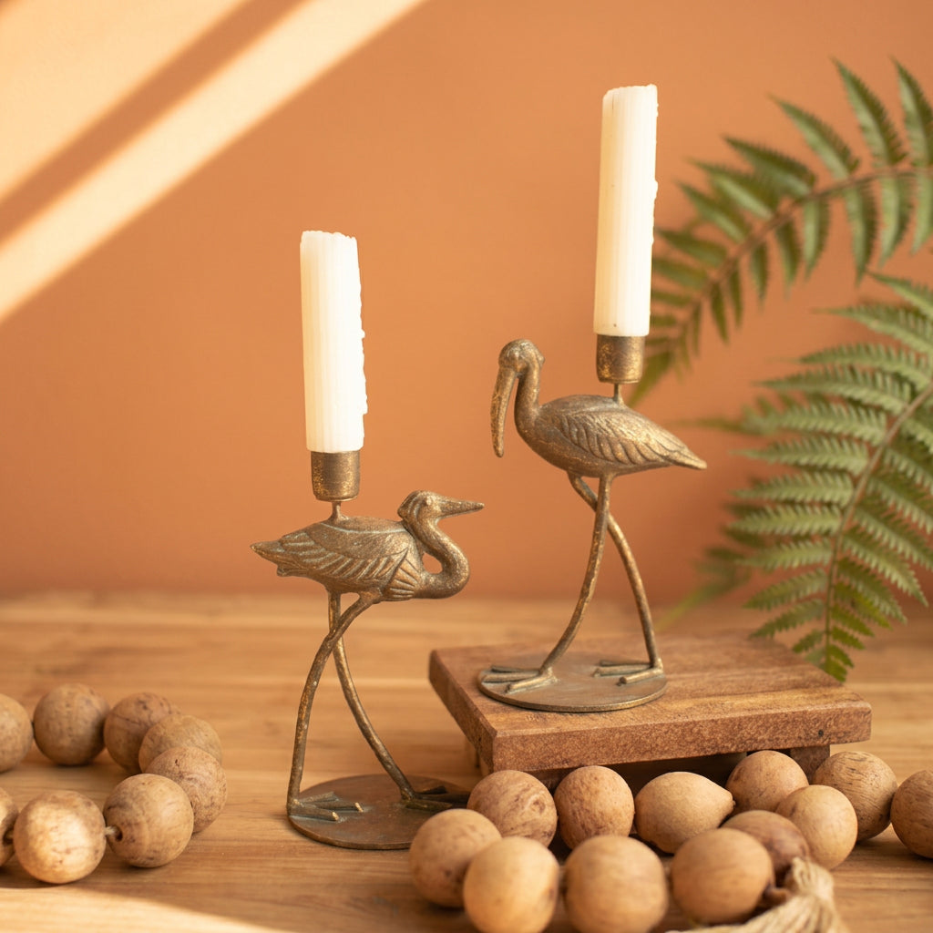 Antique brass shore bird taper holders with white candles on a wood table