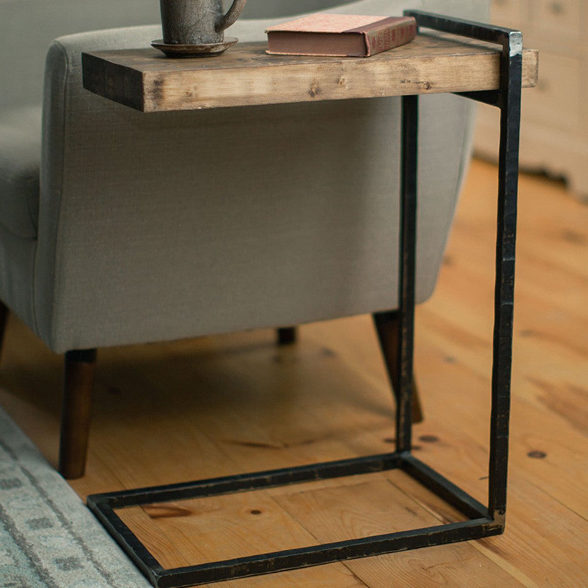Hand-forged iron C table with a warm wood top beside an upholstered chair