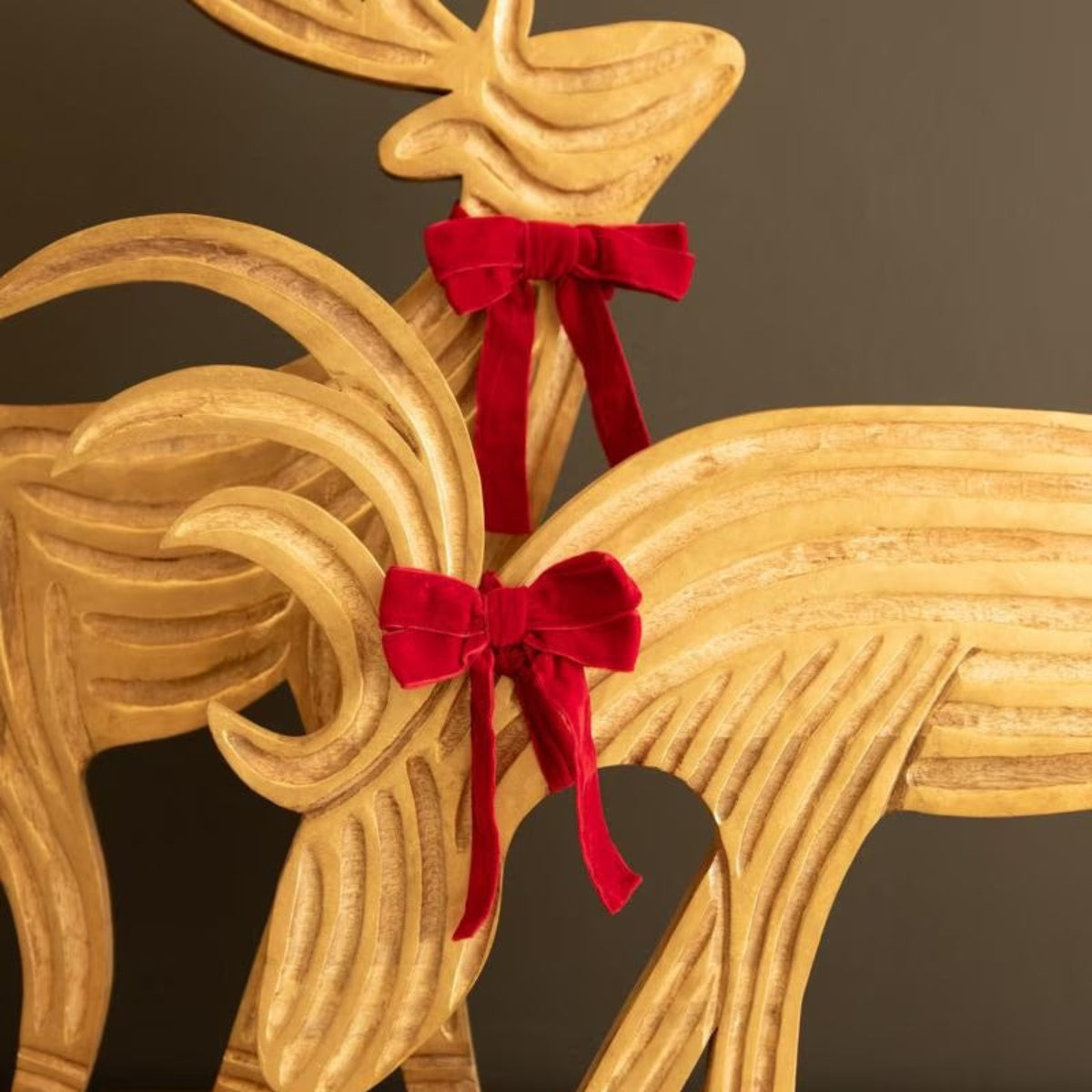 Close-up of red velvet bows and carved grain on mango wood reindeer