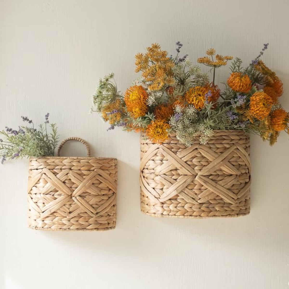 Two woven wall baskets hung on a white wall filled with dried flowers