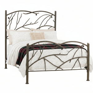 A wrought iron bed frame with a design that includes flowing branch motifs and pinecone accents, with a beige bedsheet on it.