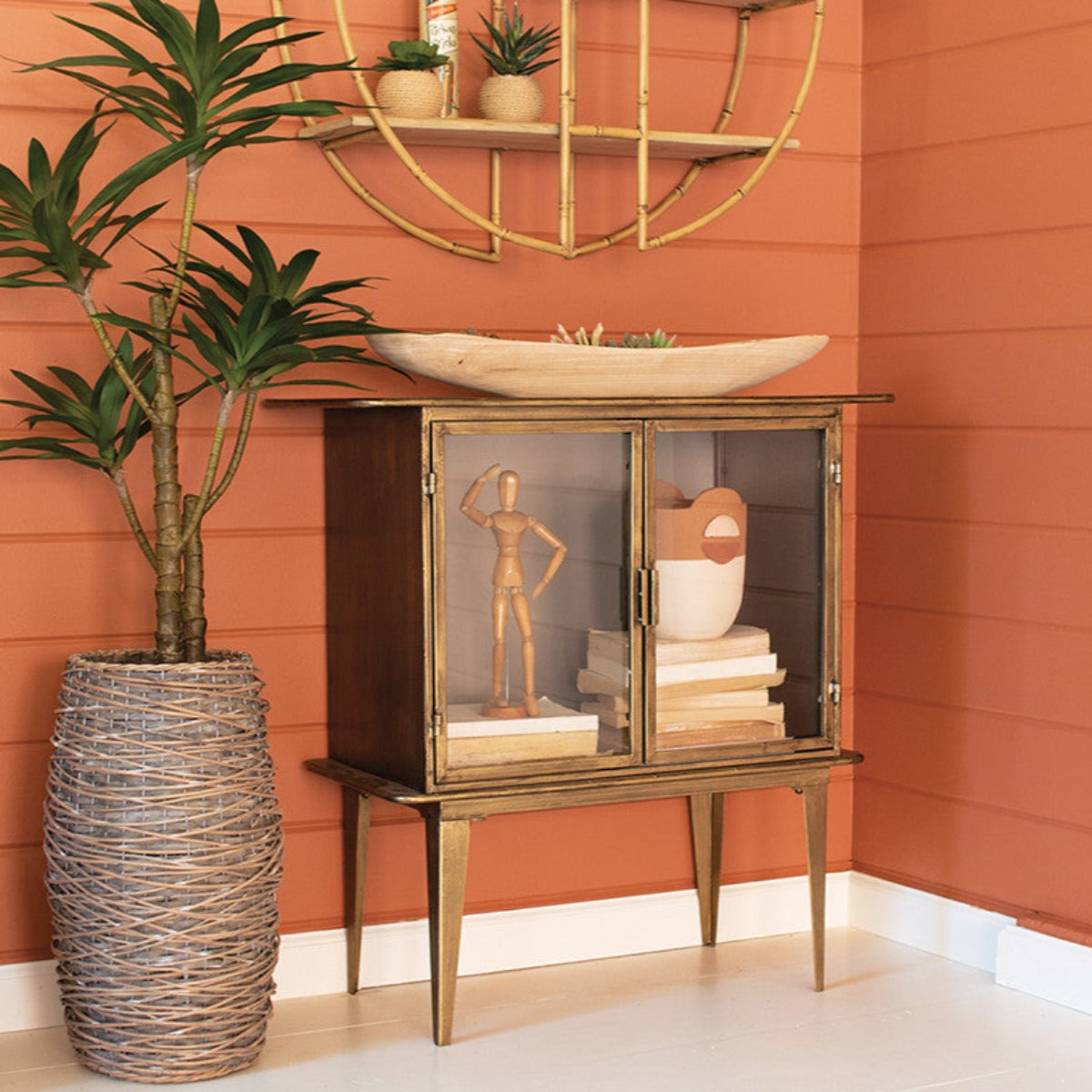 Antique brass two-door glass cabinet styled with plants against an orange wall